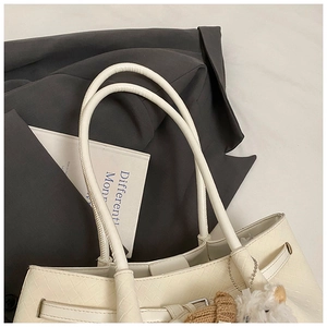 Detail of cream woven tote bag featuring large grid pattern and cute plush charm pendant