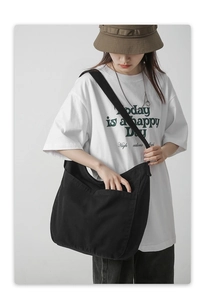 Black canvas tote bag with wide shoulder strap shown on model for casual commuting style