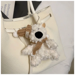 Detail of white plush bear charm with brown knit hat and scarf on a textured handbag