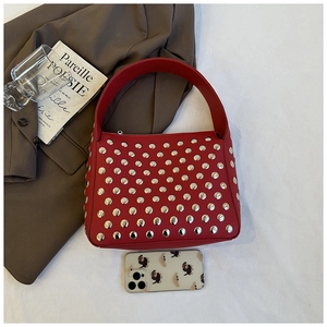 Detail of red shoulder bag featuring silver metal rivets and a wide leather handle