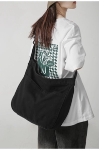 Detail of a large black canvas crossbody bag with wide shoulder strap on a model