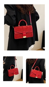 Borsa ricamata rossa con chiusura dorata e manico intrecciato su abito nero elegante