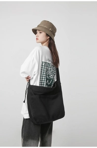 Detail of a large black canvas messenger bag on a model showing side view and large pocket