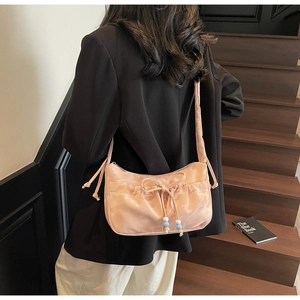 Dettaglio della borsa a spalla in raso rosa con fiocco e coulisse con perline sulla modella