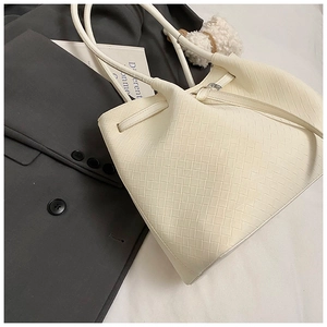 Detail of cream woven leather bucket bag with cross-weave texture and metal buckles