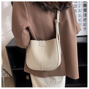Detail of cream pebbled leather bucket bag with magnetic buckle and slim shoulder strap