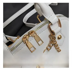Close-up of white patent leather bag with gold rivets and decorative dice chain charm