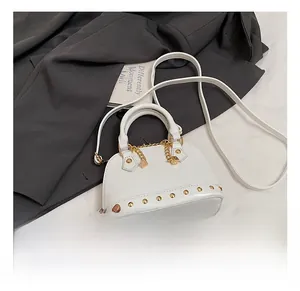 Detail shot of white shell-shaped handbag featuring gold studs and dice pendant charm