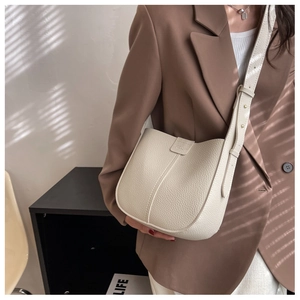 Detail of a creamy white litchi grain leather crossbody bag with golden buckle on a blazer