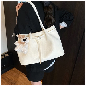 Detail of white textured bucket bag featuring a cute plush dog pendant on shoulder strap