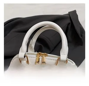 Detail view of the white patent leather shell bag with gold double zippers and metal chain