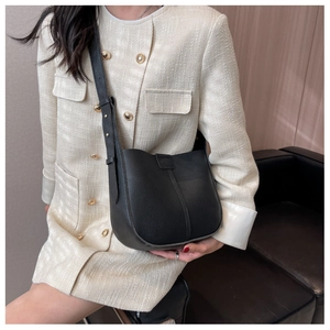 Detail of black pebbled leather bucket bag with vertical stitching on ivory jacket