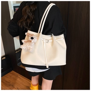 Close-up of beige woven tote bag with buckle detail and white plush bear charm