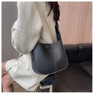 Detail of black pebbled leather bucket bag with wide strap on elegant tweed jacket