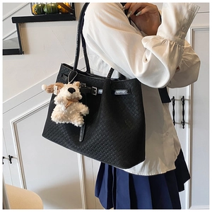 Detail view of black woven tote bag with a white plush puppy charm on a soft background