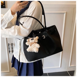 Detail of woven black tote bag featuring a white plush bear charm and slender straps