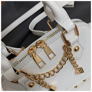 Close-up of white patent leather shell bag with gold hardware and dice charm