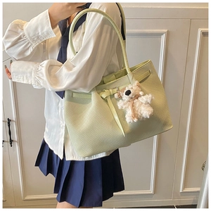Detail of mint green woven tote bag with plush bear charm showing large capacity