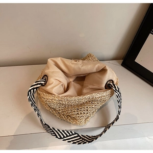 Detail view of woven straw bag with striped strap, fabric lining, and magnetic buckle