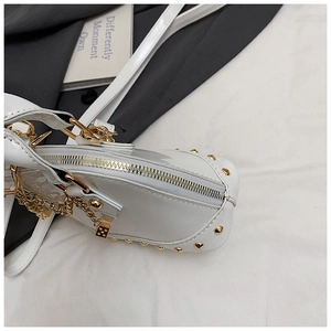 Detail of white patent leather shell bag with gold studs and dice chain pendant