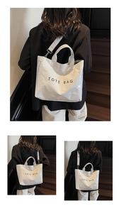 Detail of white wrinkled tote bag featuring black text print and wide fabric shoulder strap