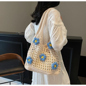 Close-up of beige crochet shoulder bag with 3D blue floral accents on white dress