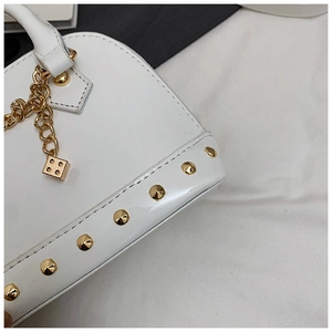 Detail of white glossy shell bag with gold rivets and unique dice charm on a chain