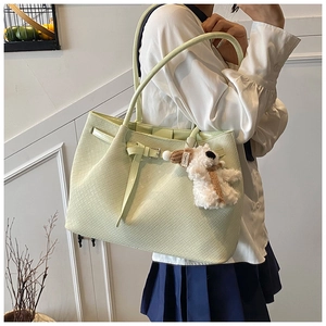 Detail of light green woven leather tote bag featuring a cute white plush puppy charm