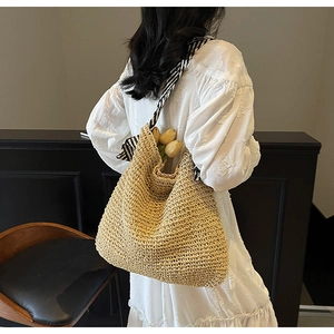 Detail of hand-woven straw tote bag featuring a striped scarf handle and natural texture
