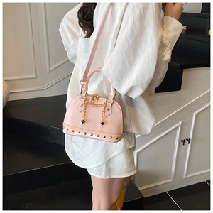 Close-up of pink patent leather shell bag with gold studs and chain details on stairs