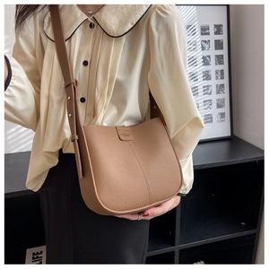 Brown lychee leather bucket bag worn as crossbody with adjustable strap on model