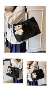 Detail of black woven tote bag featuring silver buckle strap and white plush bear charm