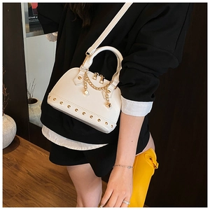 Close-up of a white shell bag featuring gold rivets, fine chain, and polished hardware