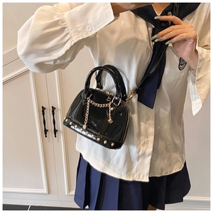 Macro detail of black patent leather shell bag with gold rivet studs and chain strap