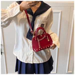 Detailed view of red patent leather shell bag with gold rivets and chain strap accents