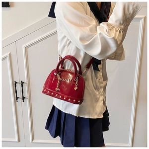 Detail of red patent leather shell bag featuring gold chain accents and stud decorations