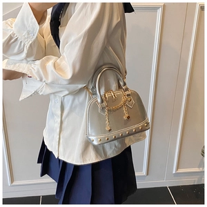 Detail of silver glossy shell bag featuring golden chain, rivet studs and double zipper