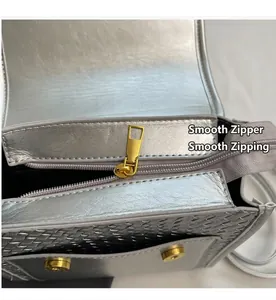 Detail of metallic silver crossbody bag with smooth golden zipper and woven texture flap