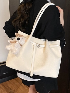 Chic beige tote bag with buckle straps and plush bear charm shown on model