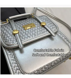 Detail of silver woven crossbody bag featuring golden logo plate and metallic studs