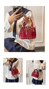 Detail of red patent leather shell bag with gold chain and metal rivets on smooth surface