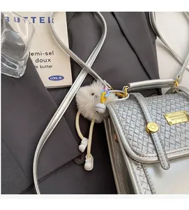Detail of silver woven handbag with gold metal plaque and plush monster charm