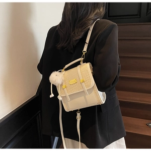 Detail of beige woven crossbody bag with metal plaque and white fur pompom pendant