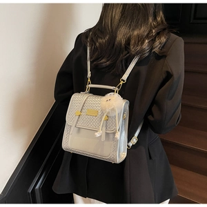 Detail of silver-grey embossed backpack with gold logo plaque and white plush pendant