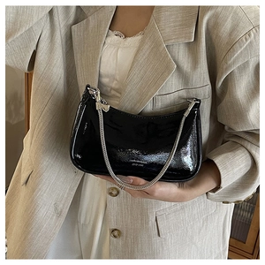 Detail of glossy black patent leather bag with silver chain strap and heart pendant