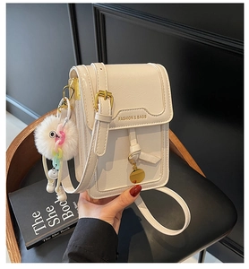 Close-up of a white textured crossbody bag with gold FASHION lettering and pom-pom