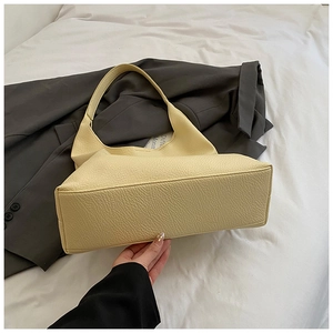 Close-up of pale yellow lychee leather shoulder bag with smooth texture on grey blazer