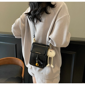 Detail view of black crossbody phone bag with fashion logo and fluffy charm on model