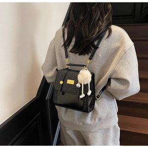 Detail of black woven texture and leather backpack with white fluffy pompom charm