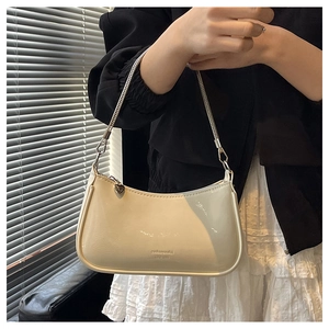 Detail of creamy white patent leather underarm bag with embossed text and heart charm
